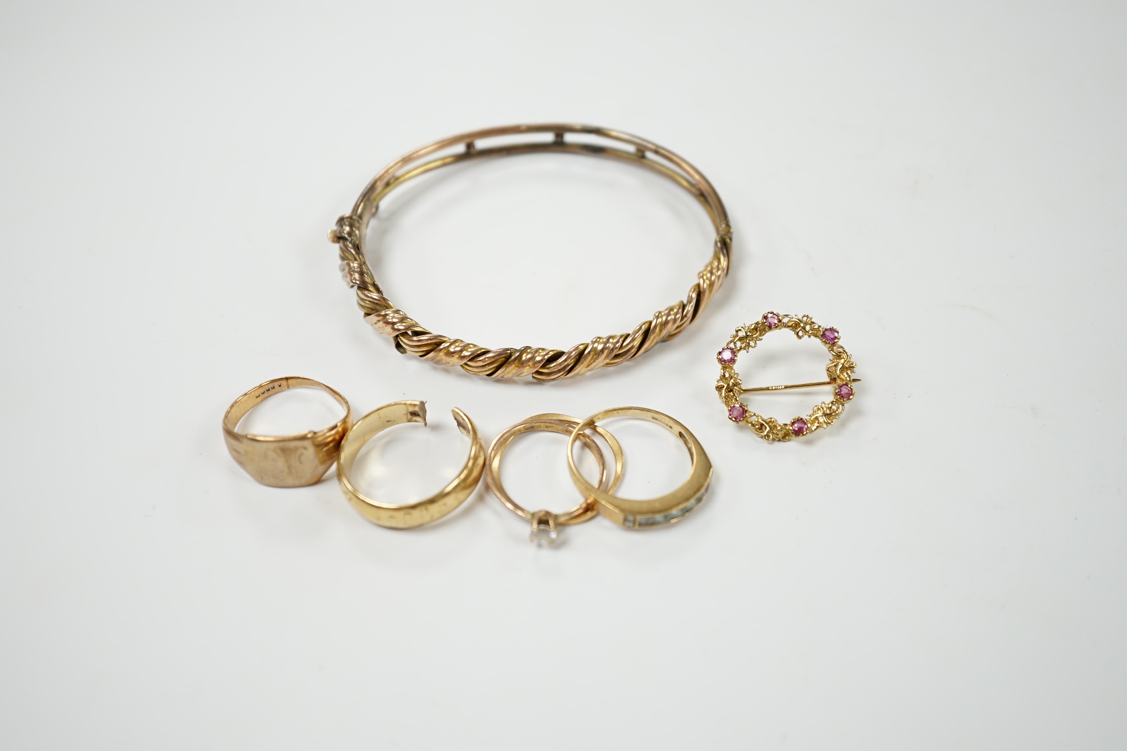 An early 20th century 9ct hinged bangle, three assorted 9ct gold rings and a modern 9ct gold and gem set brooch and two other yellow metal rings, gross weight 23.2 grams. Condition - poor